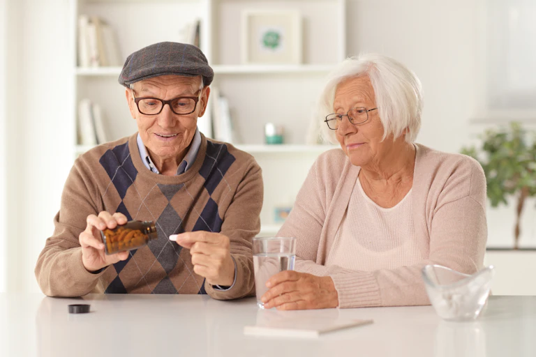 Elderly couple sit at a table at home and take vitamin pills