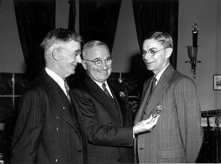 Black-and-white photo of Vannevar Bush, Harry Truman and James Conant smiling in suits, Truman presenting Conant a medal