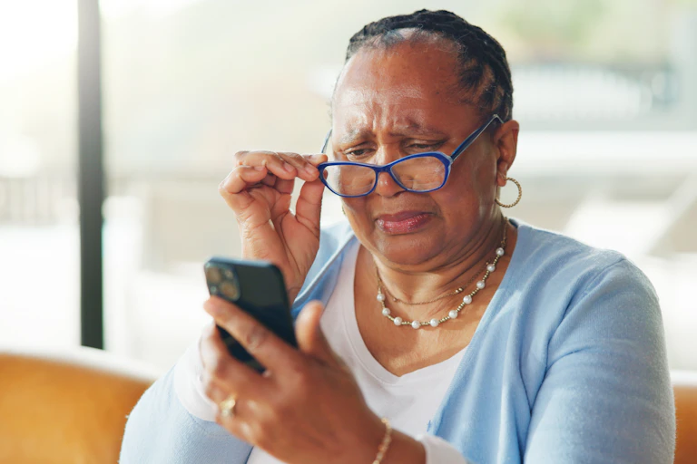 older woman lowers her glasses to look quizzically at her phone