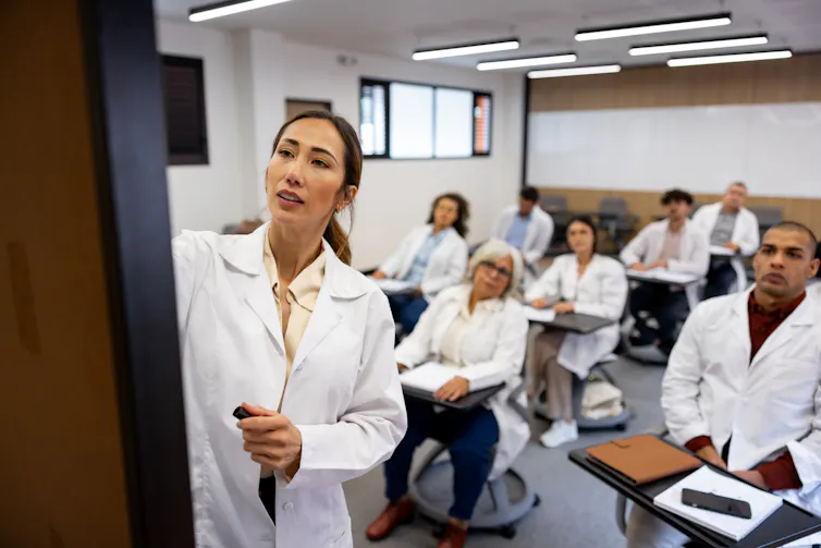 Woman writing on the board while teaching a class to a group of people in white coats