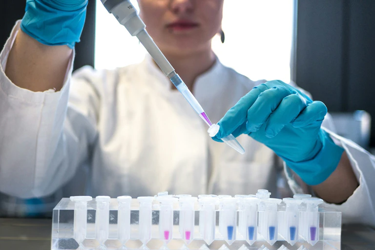 a person in a white lab coat using a syringe to take a liquid from a vial