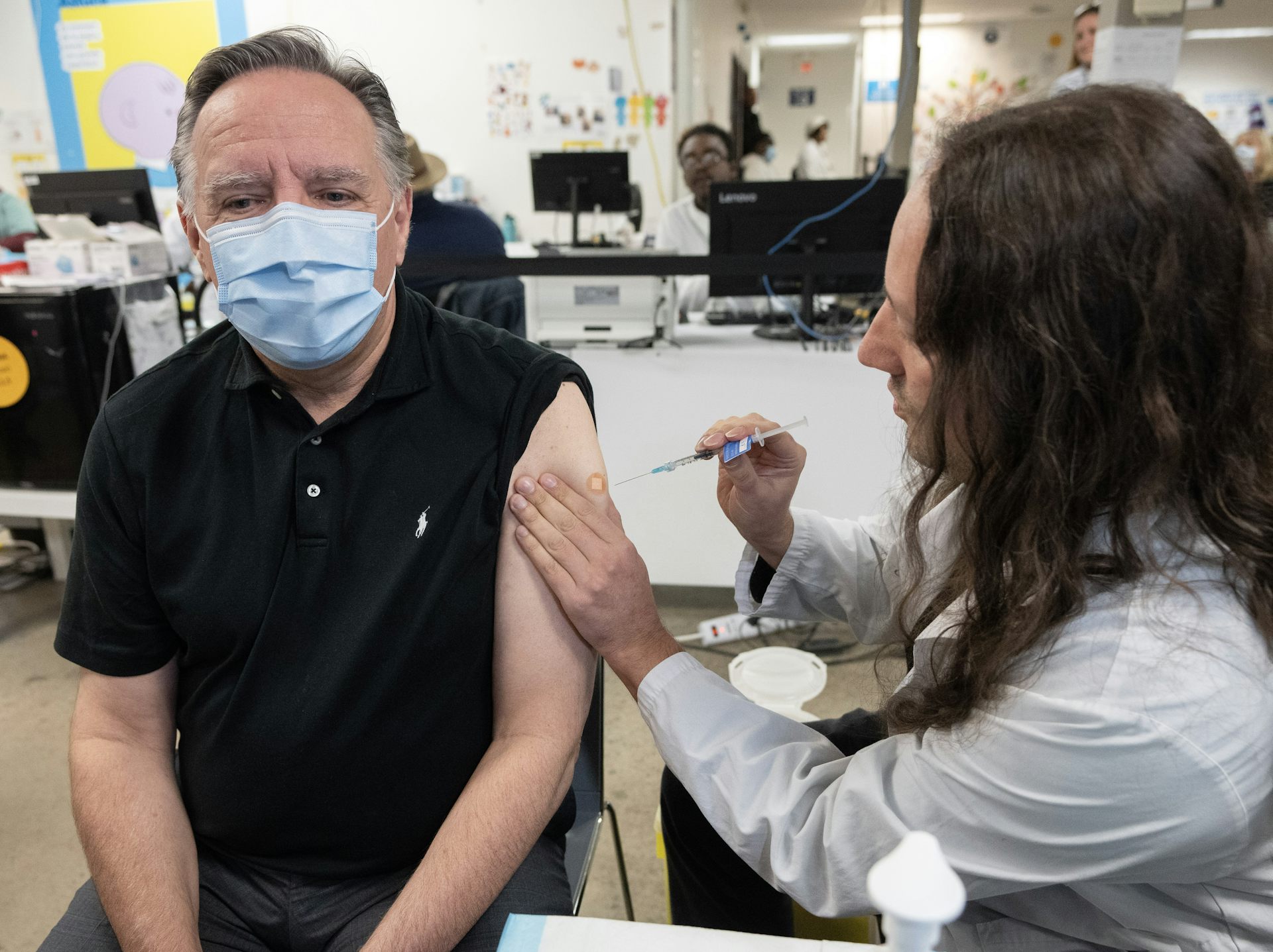 Una enfermera inyecta al primer ministro de Quebec, François Legault, en su brazo izquierdo. Lleva una máscara médica azul.