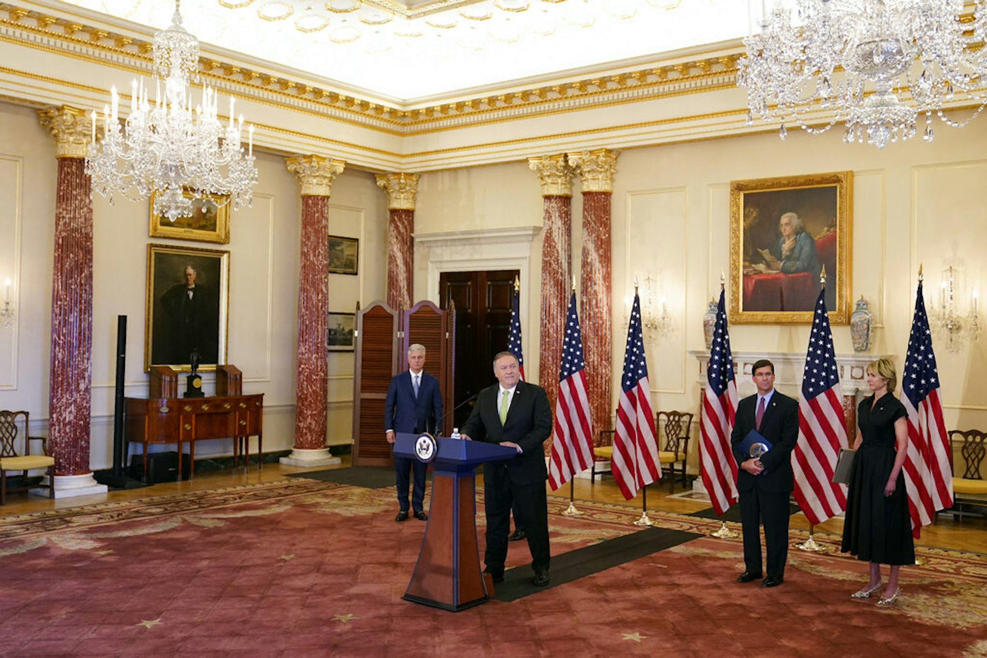 A man in a suit stands at a podium during a press conference.