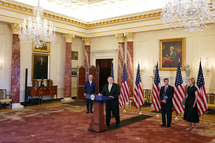 A man in a suit stands at a podium during a press conference.