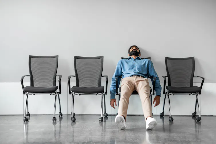 Bored man sitting back on row of chairs.