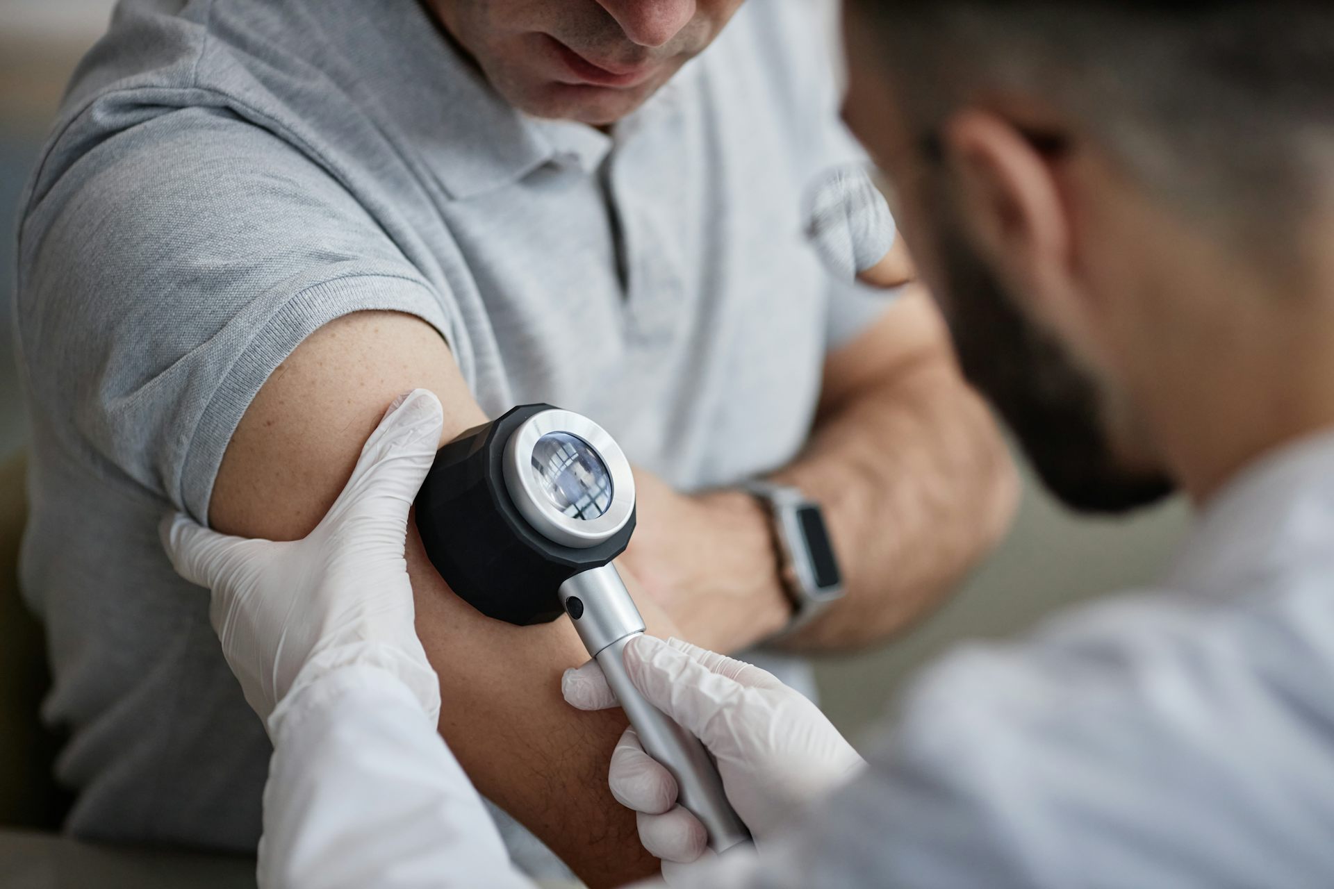 A middle-aged man has his arm examined for signs of melanoma by a male doctor.
