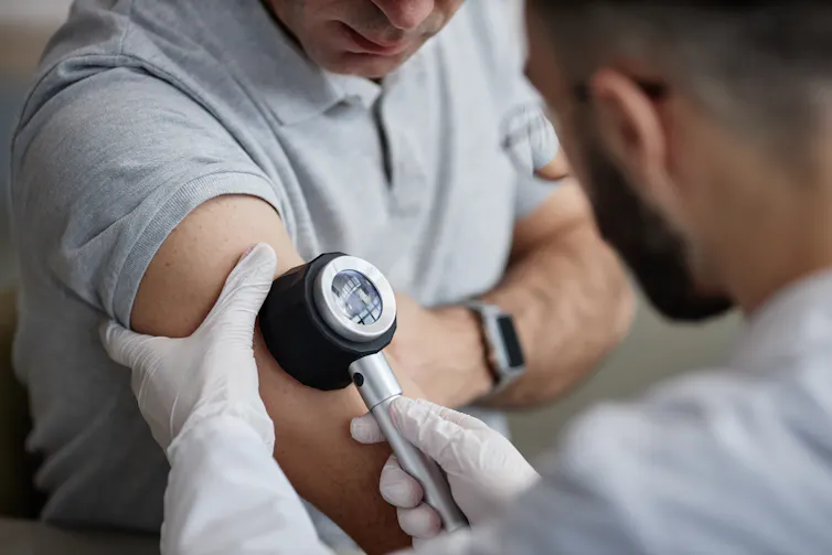 A middle-aged man has his arm examined for signs of melanoma by a male doctor.