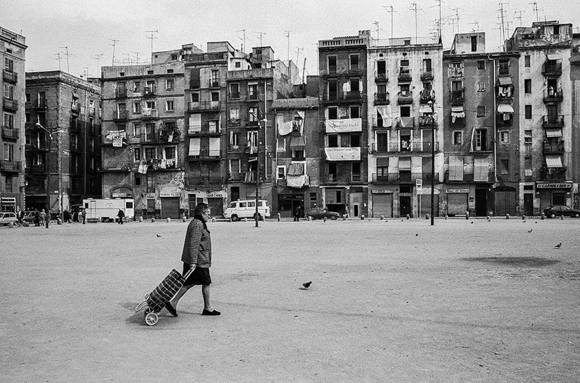 Una dona camina pel carrer davant d'edificis antics en una imatge en blanc i negre.