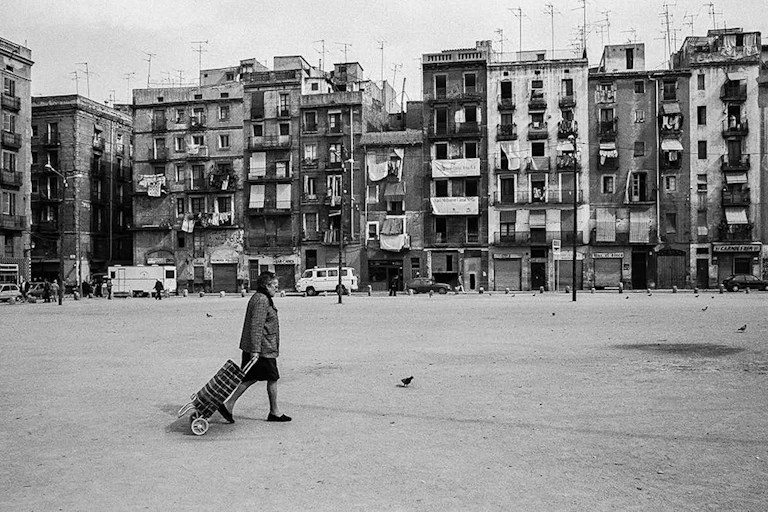 Una dona camina pel carrer davant d'edificis antics en una imatge en blanc i negre.