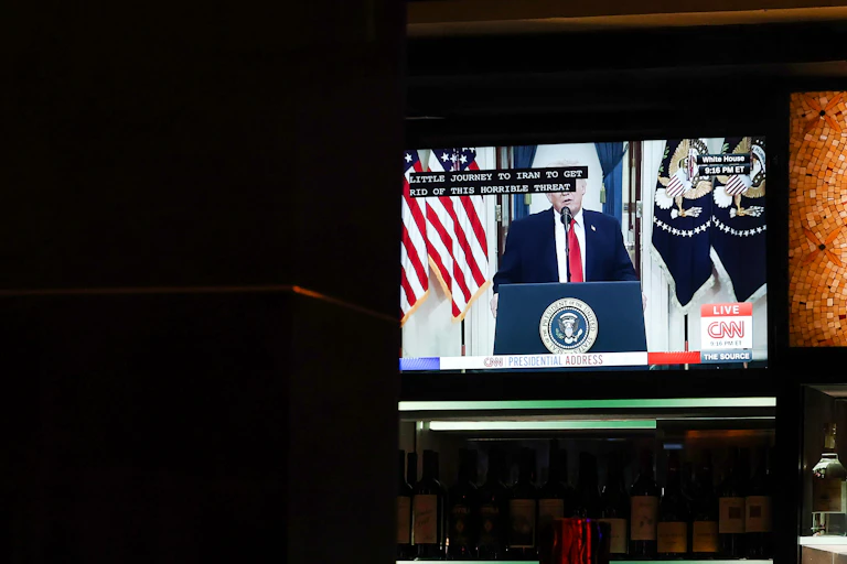 A TV screen in a restaurant displaying a man in a suit and tee making a public address.
