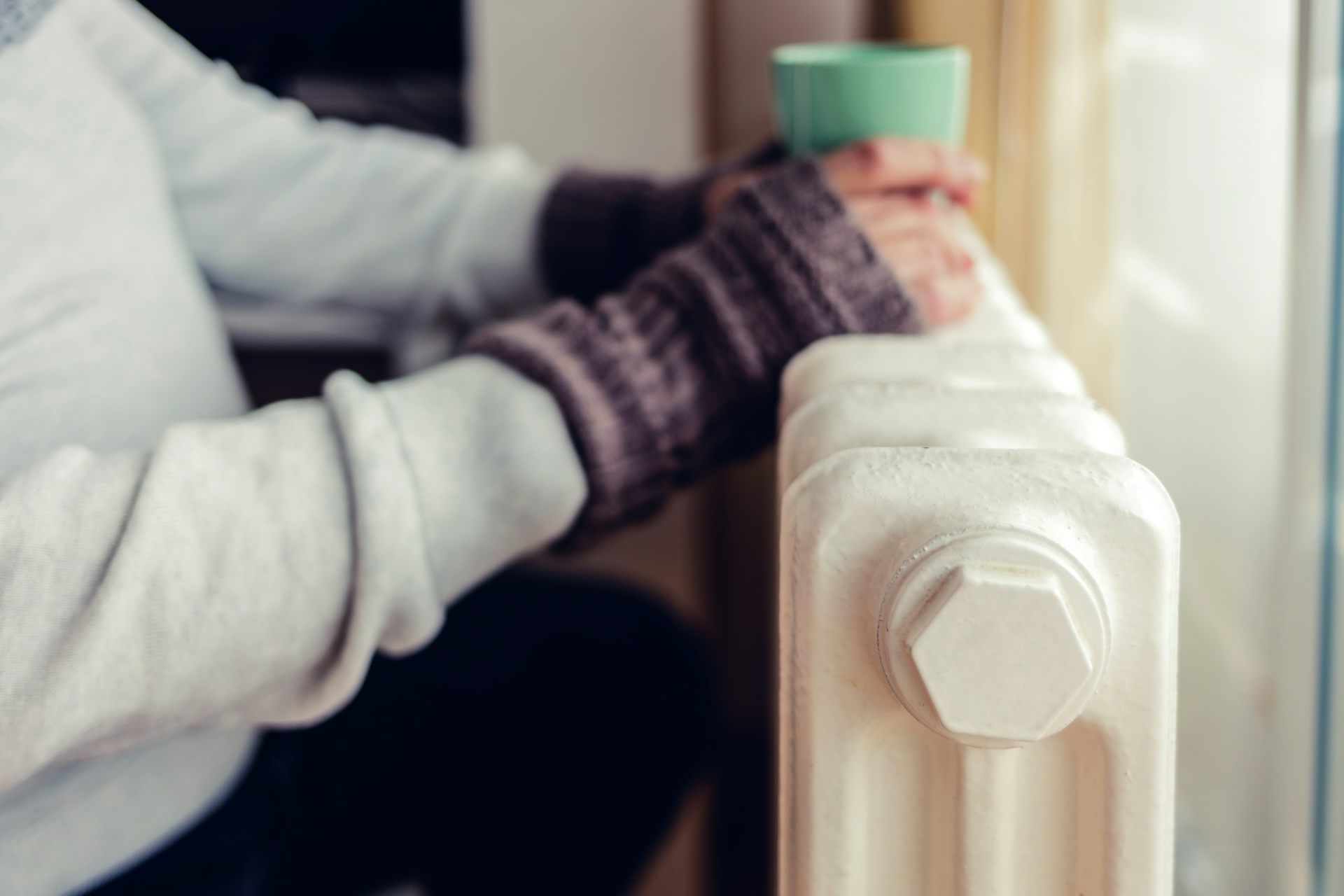 Close up of someone resting their hands and hot drink on a radiator