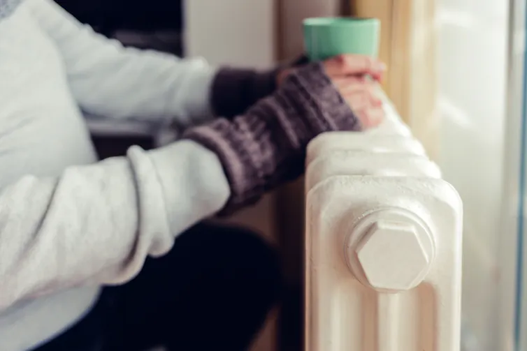 Close up of someone resting their hands and hot drink on a radiator