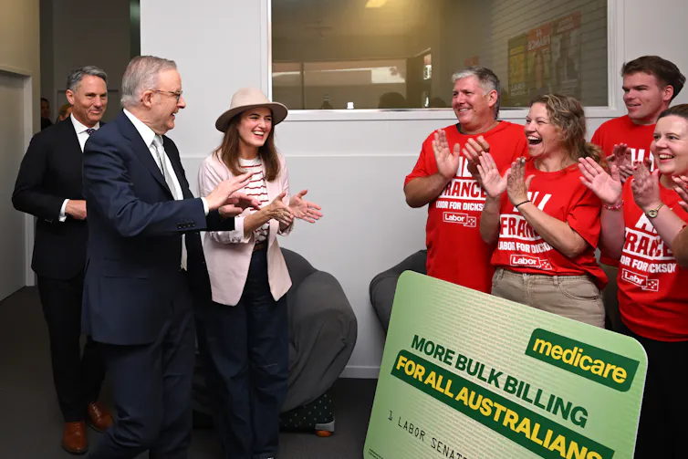 Albanese and a woman clapping as they greet supporters wearing red t-shirts and with a Medicare care that says more bulk billing for all australians