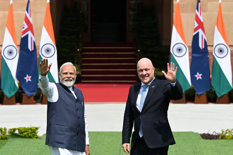 Indian Prime Minister Narendra Modi and New Zealand Prime Minister Christopher Luxon waving in front of their country flags
