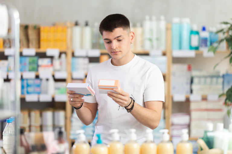 A man looks at two small boxes of an unknown product in a shop.