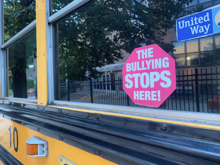 A red sign in the window of a yellow school bus says the bullying stops here!