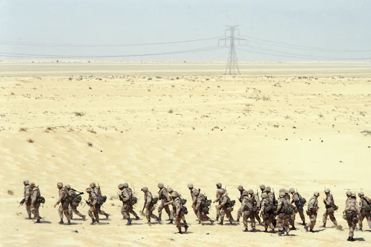 Soldiers are seen walking in a line in the desert.