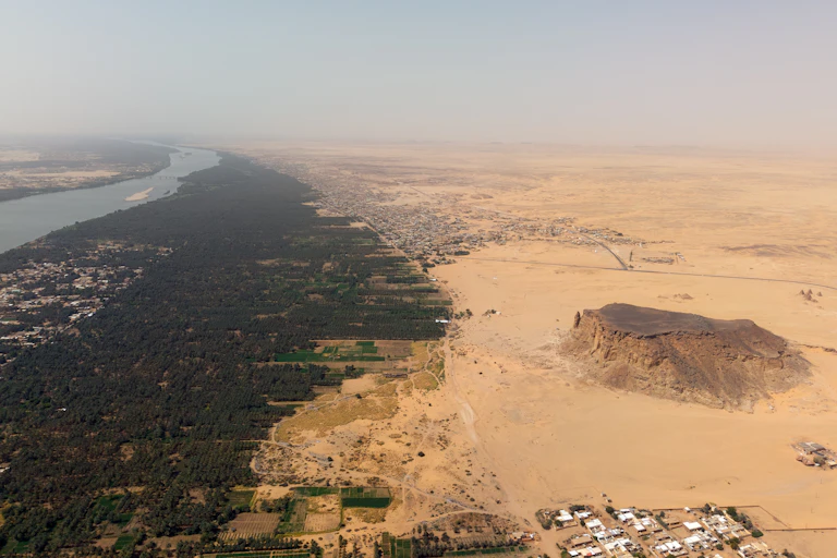 A flat mesa rises out of sandy ground with river flowing in the distance