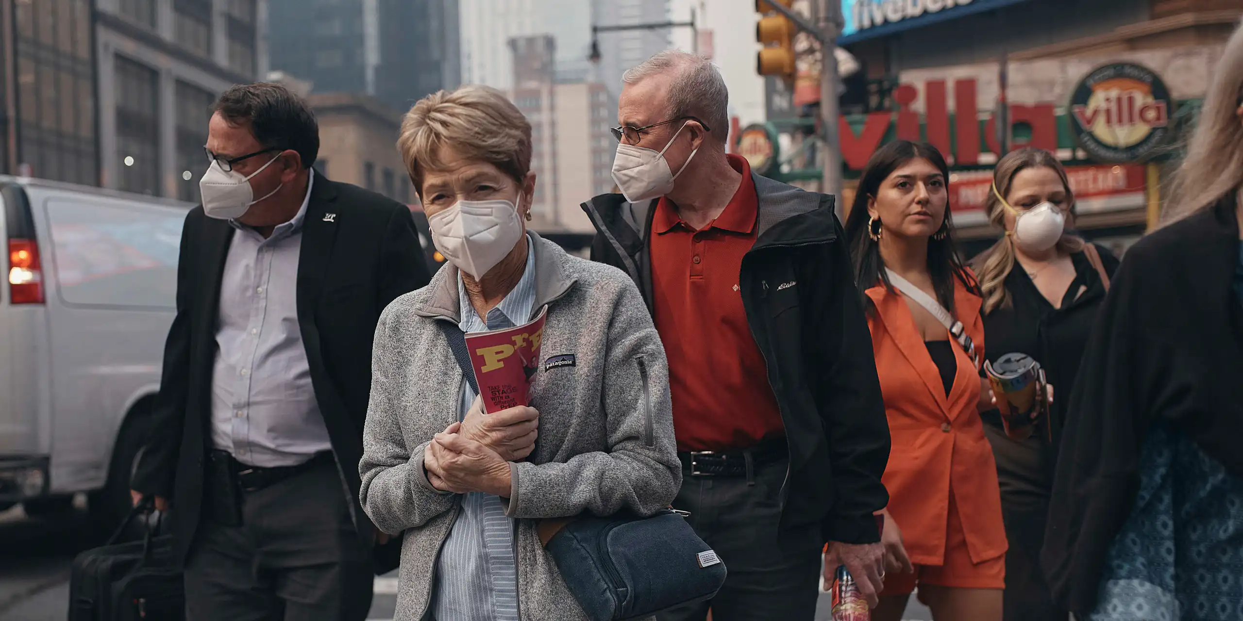 People walk along a city street wearing masks
