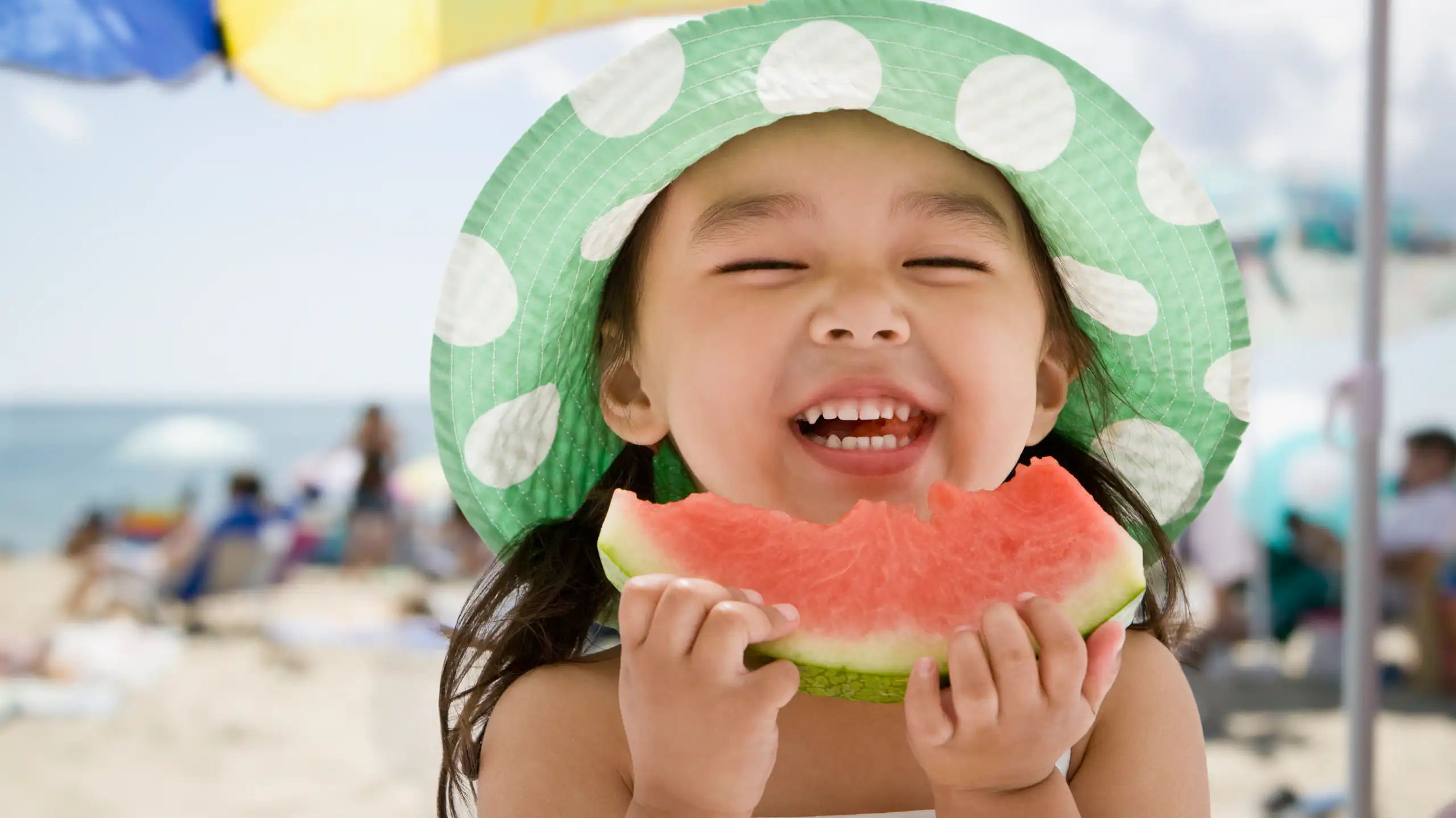 Une petite fille mange de la pastèque en souriant.