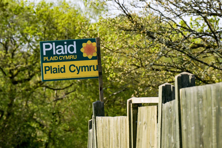 single poster for plaid cymru attached to a fence with trees in the background