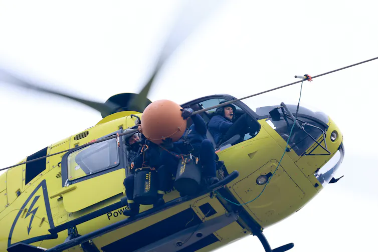 ¿Qué son esas bolas naranjas en algunas líneas eléctricas? 3 Personas asomadas a un helicóptero trabajan con una bola naranja montada sobre un cable con corriente