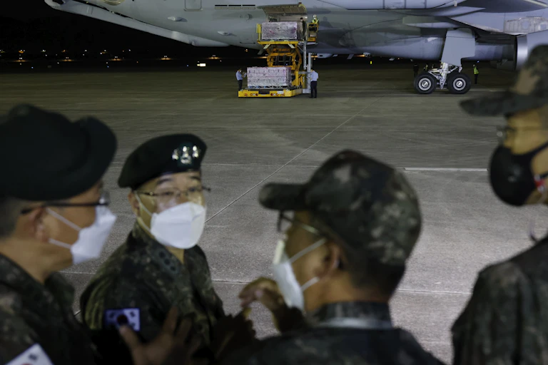 A group of people with caps and with face masks on stand in front of an airplane