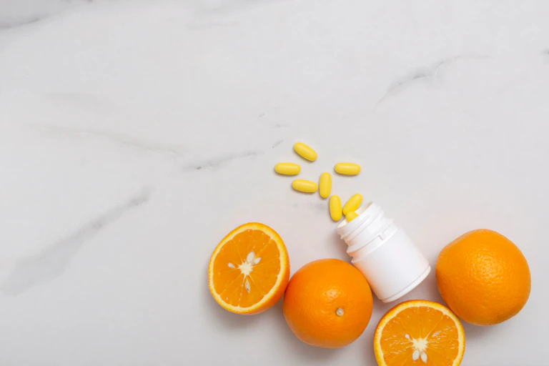 Vitamin C pills spilling out of a bottle, surrounded by oranges.