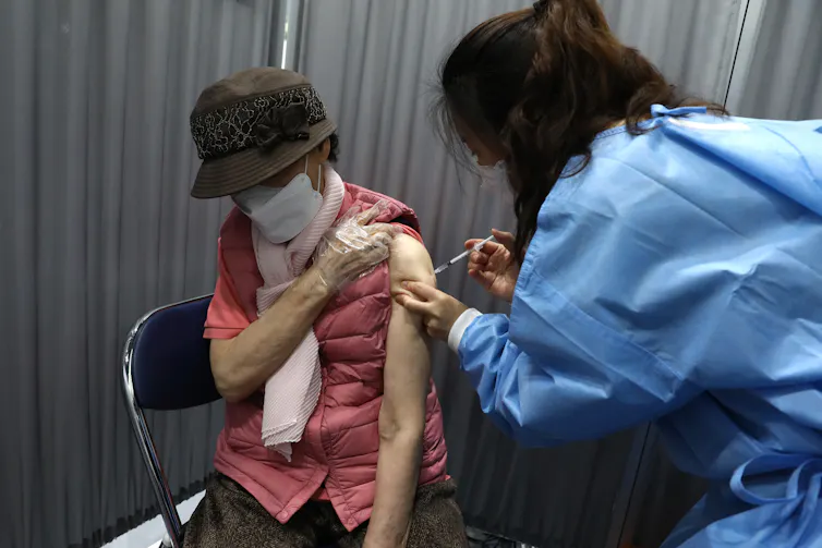 A nurse administers a vaccine shot to an elderly lady.
