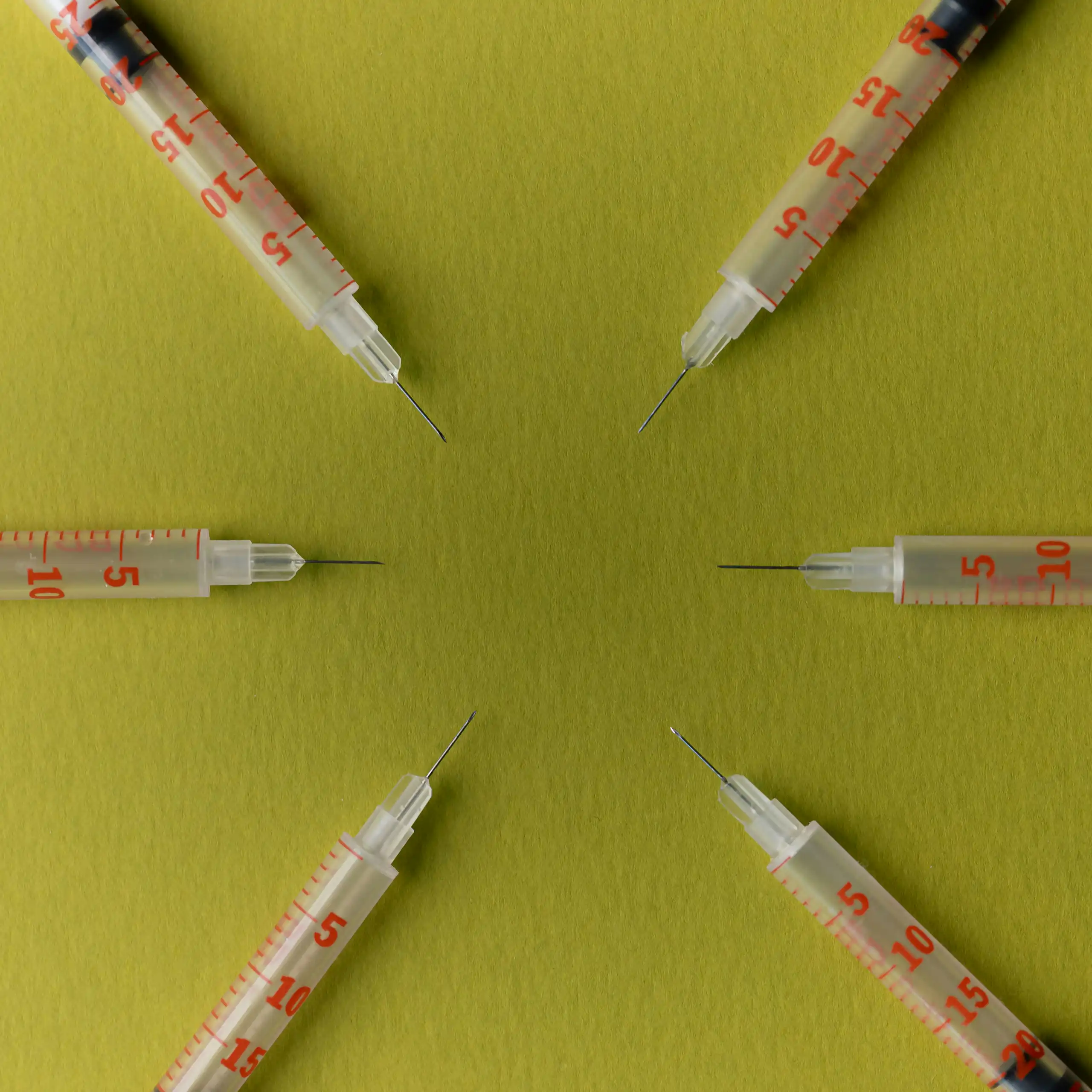Six syringes arranged in a circle pointing inward against a yellow background