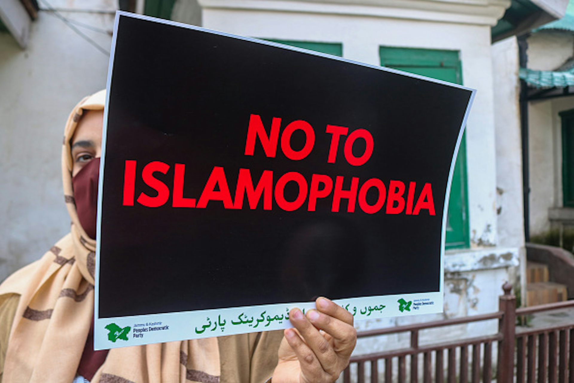 A woman wearing a headscarf and face mask holds a sign