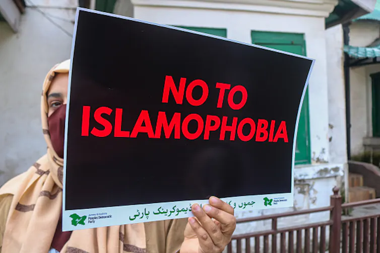 A woman wearing a headscarf and face mask holds a sign