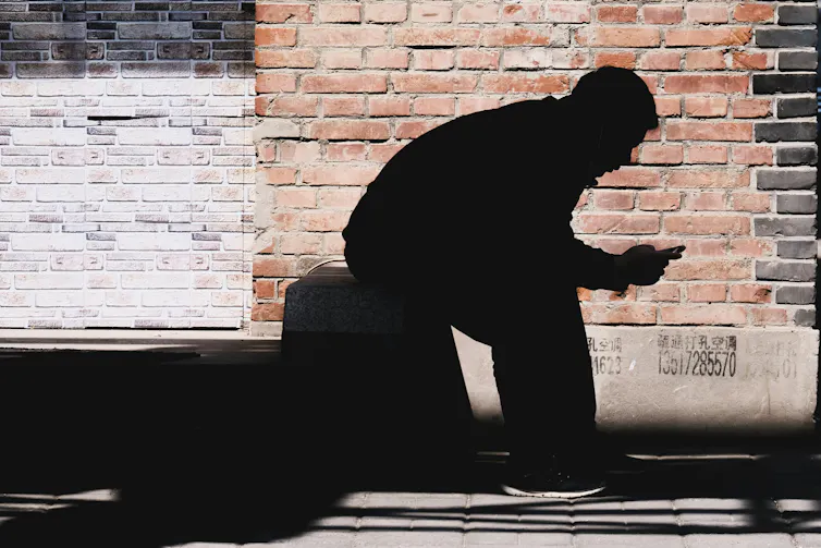 Silhouette of a man sitting down looking at a phone