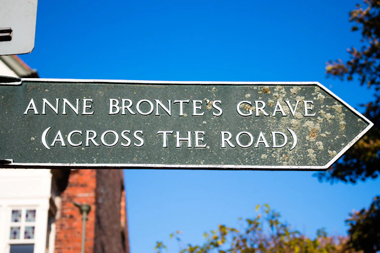A sign post to Anne Brontë's grave in Scarborough against a bright blue sky.