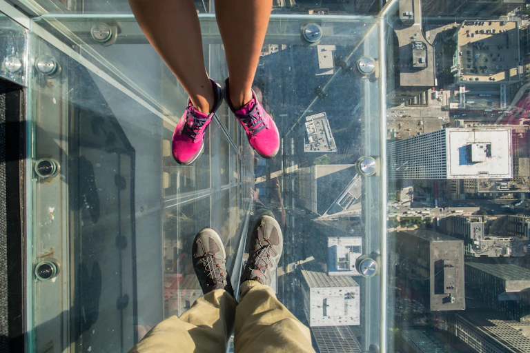 Tourists posing on a glass floor in a skyscraper.