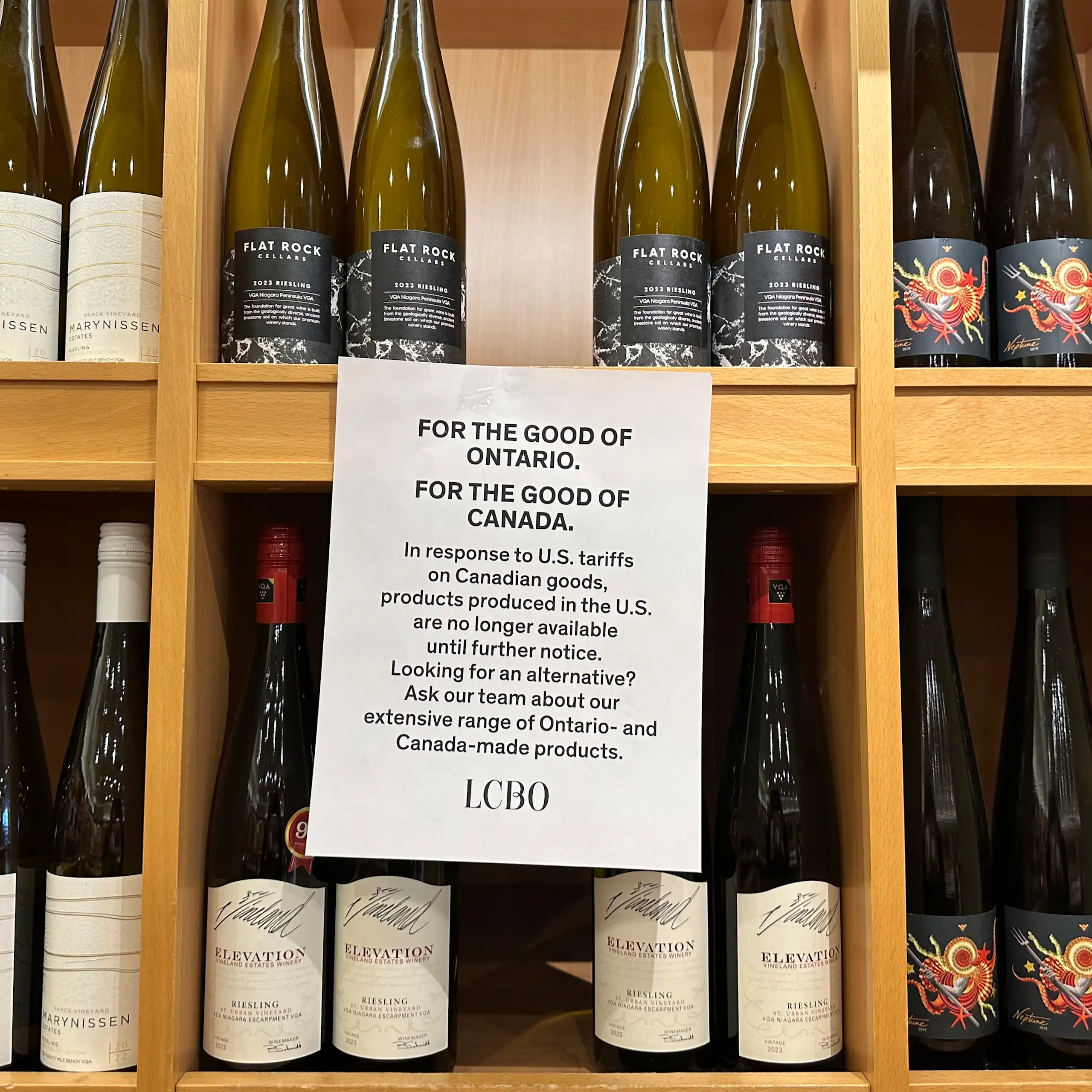 Rows of wine bottles are displayed on shelves with a sign that say U.S. products are no longer available at this Canadian store