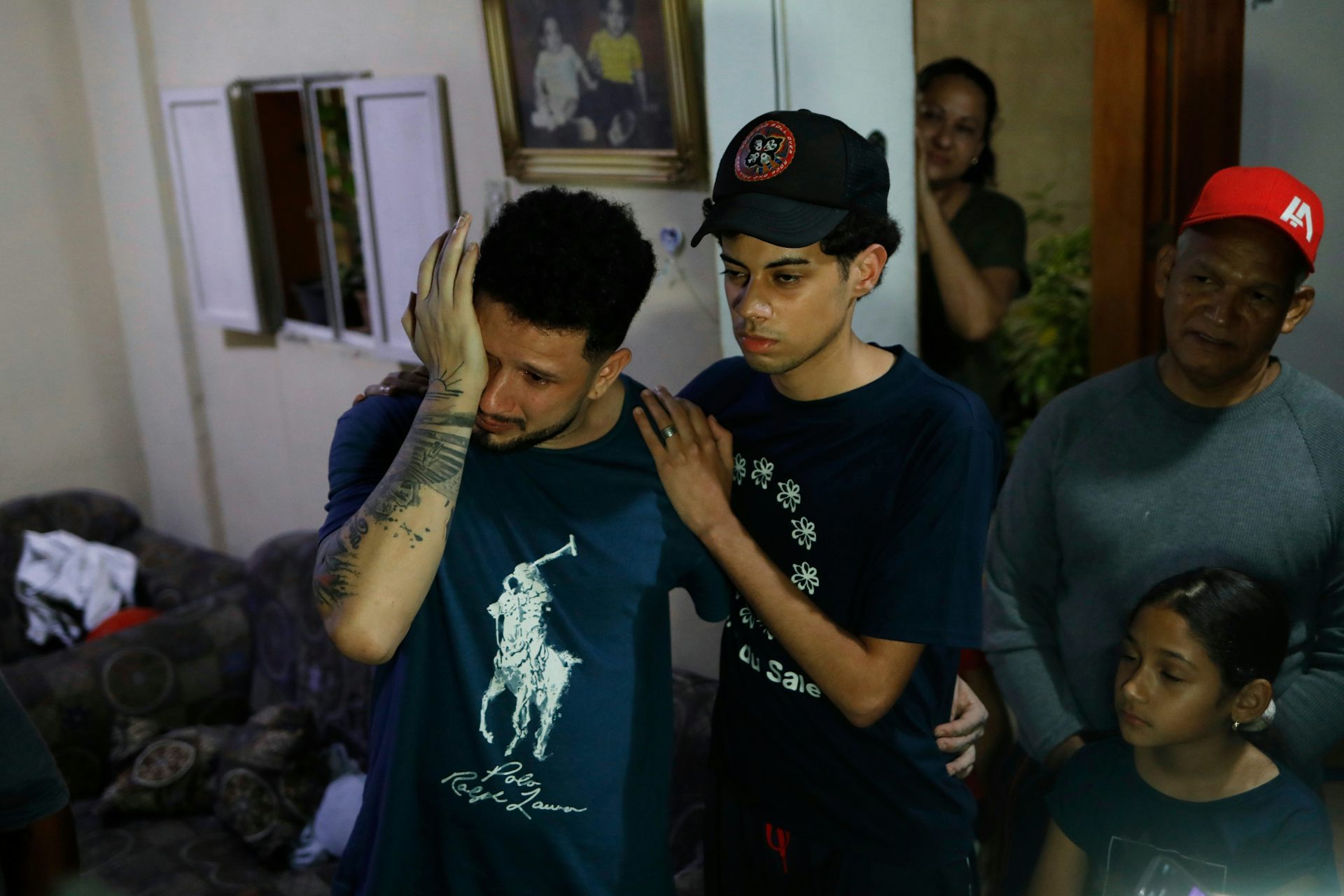 Un hombre de cabello oscuro se seca los ojos mientras un adolescente lo abraza.