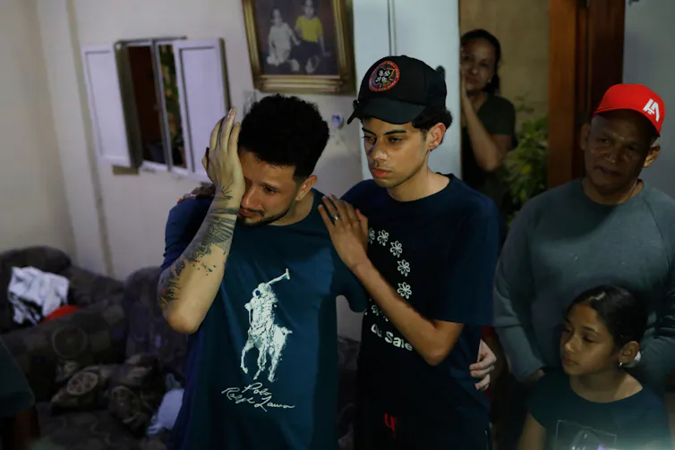 A dark-haired man wipes his eyes as a teenaged boy embraces him.