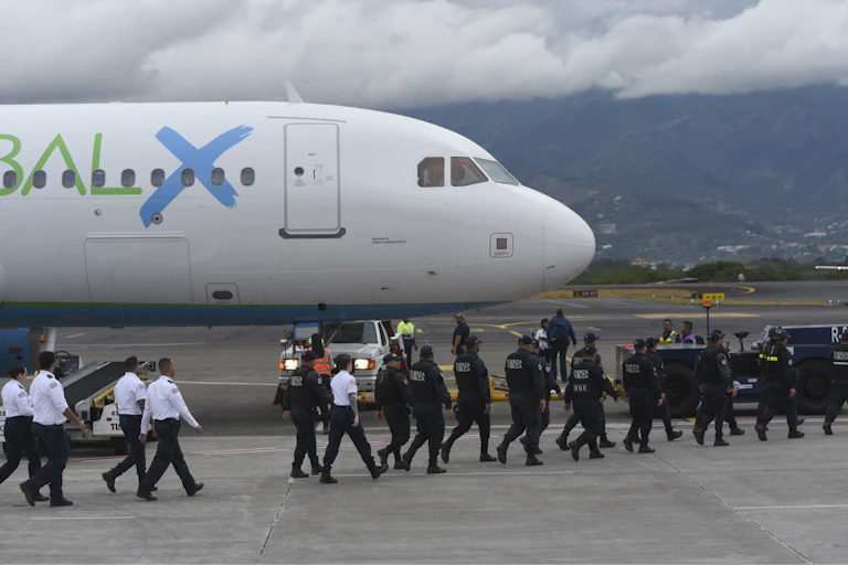 A line of security agents approach an airplane on a tarmac.