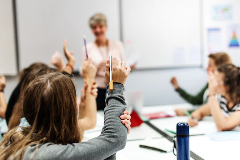 Teacher in classroom with pupils raising hands