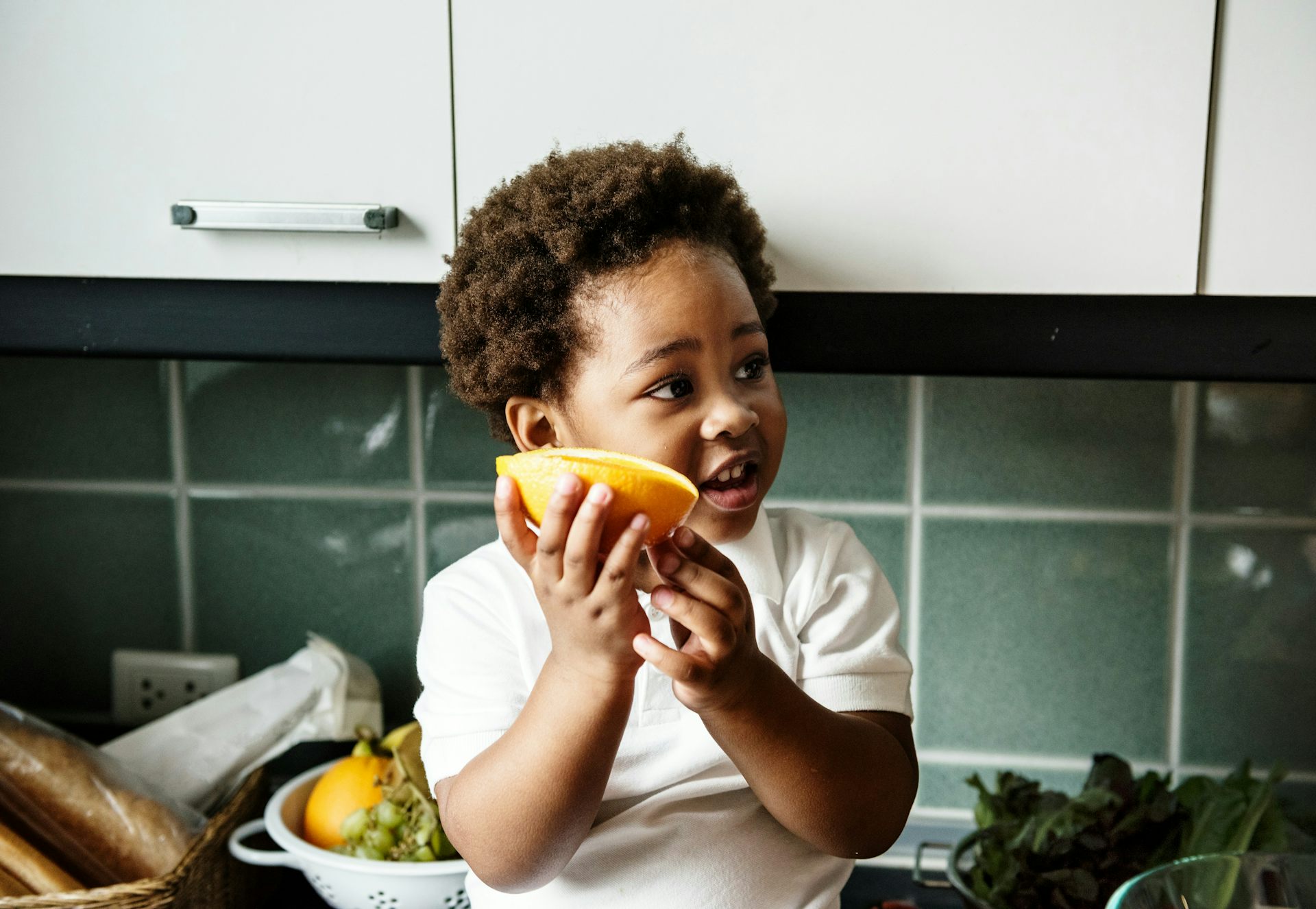 Un niño negro sonríe y sostiene un segmento de naranja.