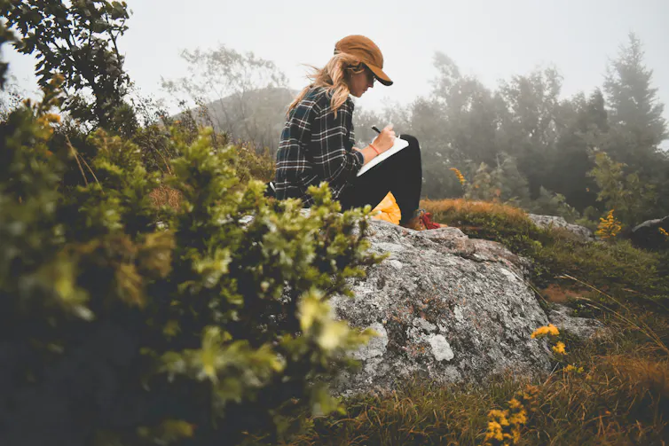 A woman sitting outdoors writing in a journal.