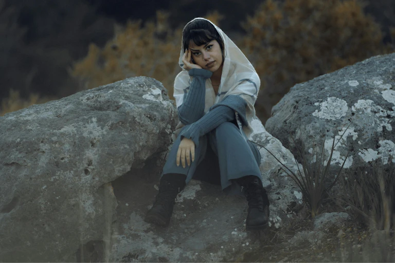 A woman sits on a grey rock.