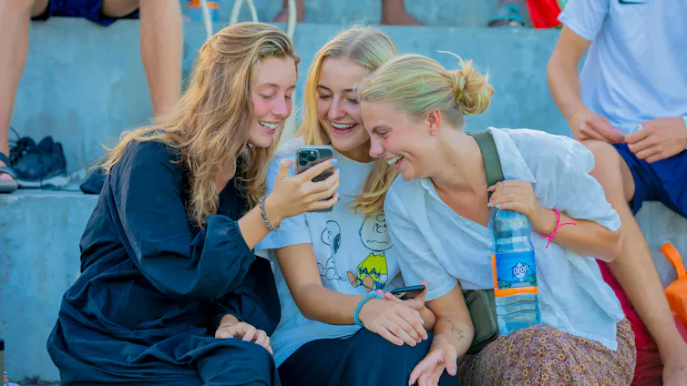 Three women sharing a joke looking at a phone screen.