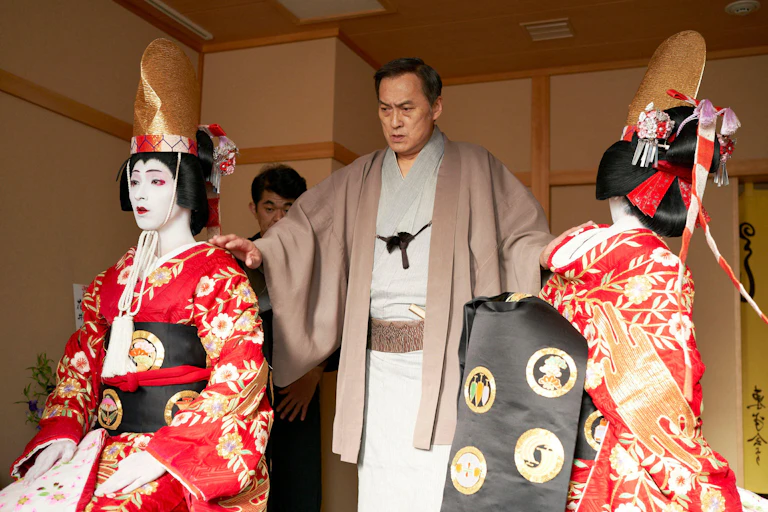 Two kabuki actors in full makeup with a director between them