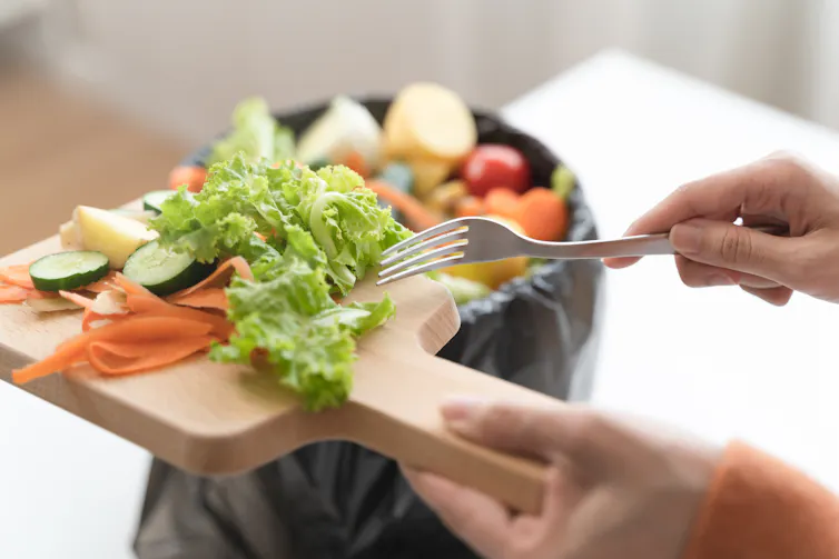 hand scraping food waste from chopping board into bin