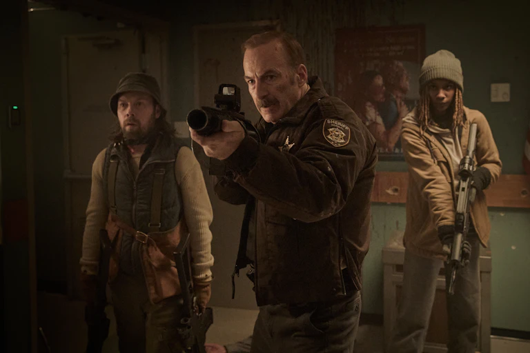 A US sheriff with a huge gun and two sidekicks in a dark room.