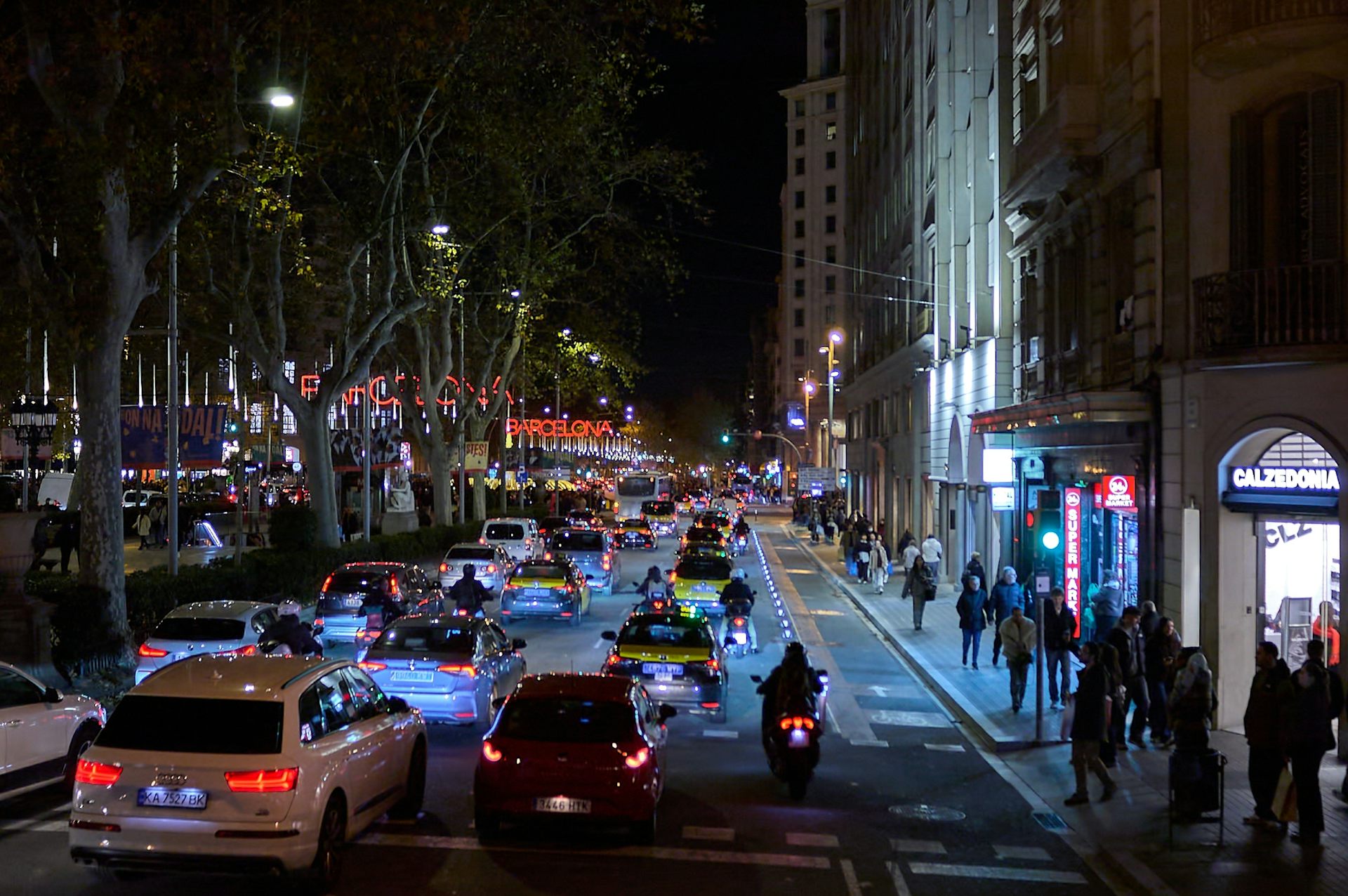 Molt de tràfic i gent a un carrer amb edificis, de nit.