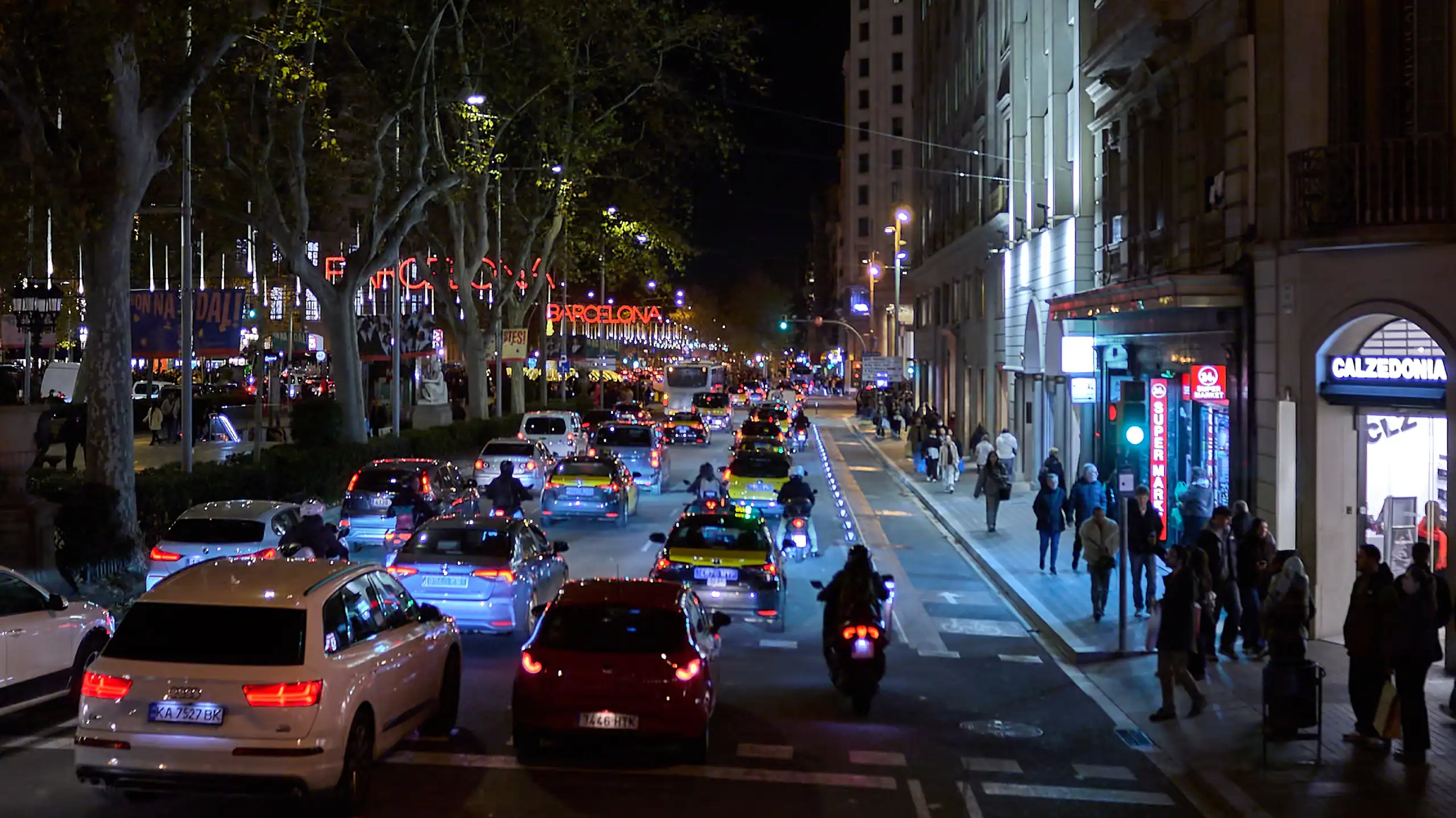 Molt de tràfic i gent a un carrer amb edificis, de nit.