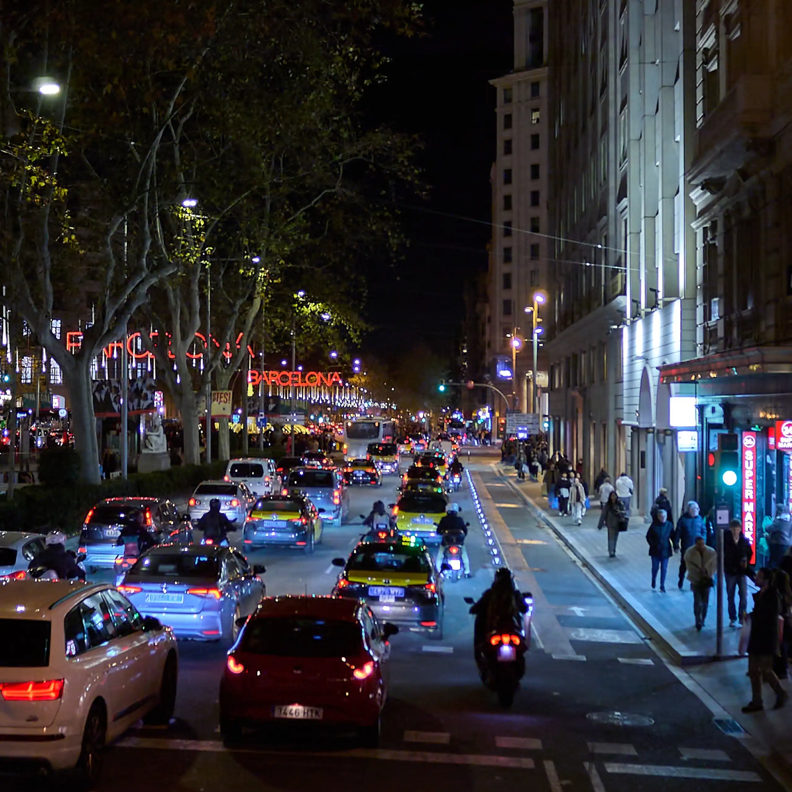 Molt de tràfic i gent a un carrer amb edificis, de nit.
